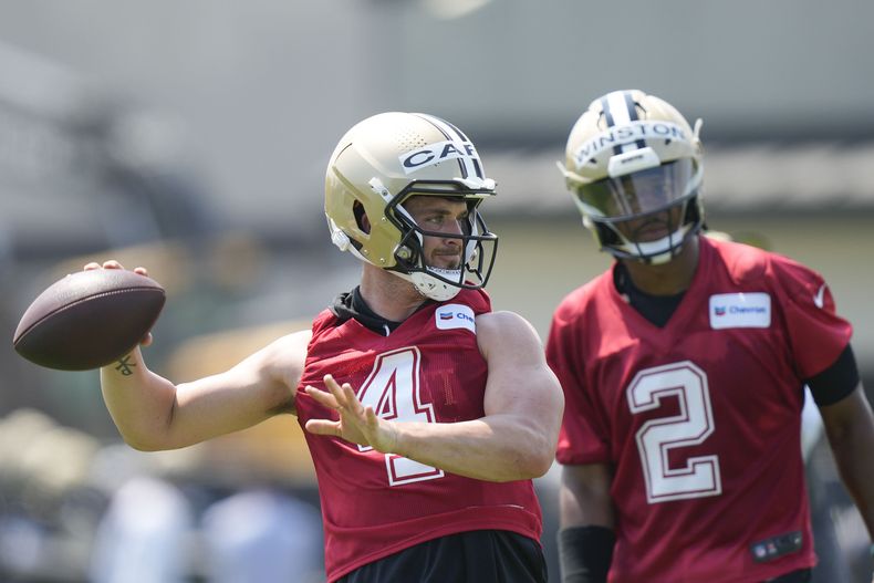 Derek Carr, quarterback de los Saints de Nueva Orleans, lanza el balón mientras que Jameis Winston (2) observa durante un entrenamiento de la NFL, en Metairie, Louissiana, el martes 23 de mayo de 2023. (AP Photo/Gerald Herbert)