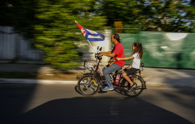 Cubanos se trasladan en una bicicleta eléctrica llevando una bandera cubana después de participar en una celebración por el Día del Trabajador en La Habana, Cuba, el viernes 5 de mayo del 2023. (AP Foto/Ramón Espinosa)